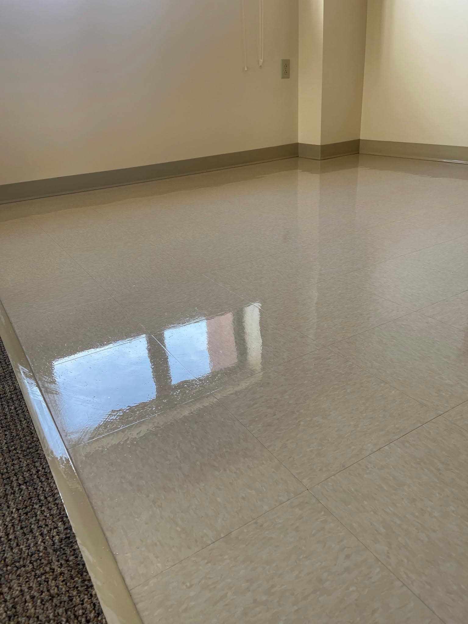 Highly polished beige floor tiles in an empty room reflecting light from a window.